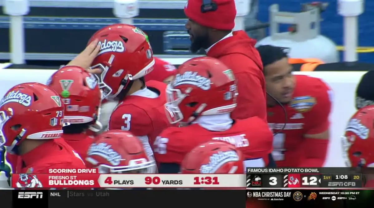A group of Fresno State Bulldogs football players in red uniforms and helmets huddle together on the sidelines during a…