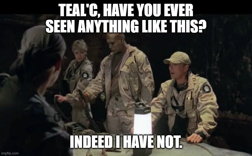 A still from the TV show Stargate SG-1 shows four characters in military-style uniforms gathered around a table. One…