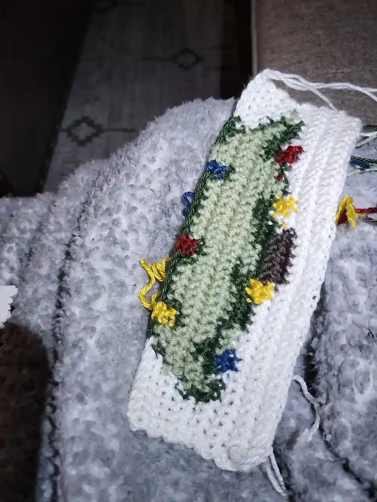A handmade crocheted item, likely a small pouch or stocking, features a green central panel with colorful embroidered…