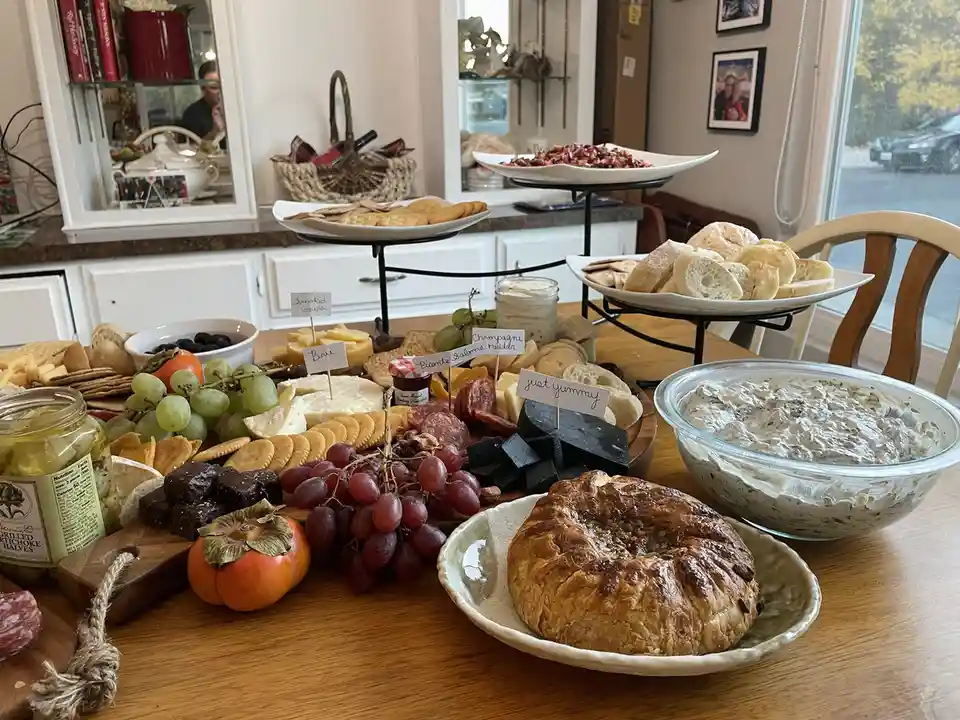 A lavish charcuterie board is displayed on a wooden table, featuring an assortment of cheeses, meats, grapes, crackers…
