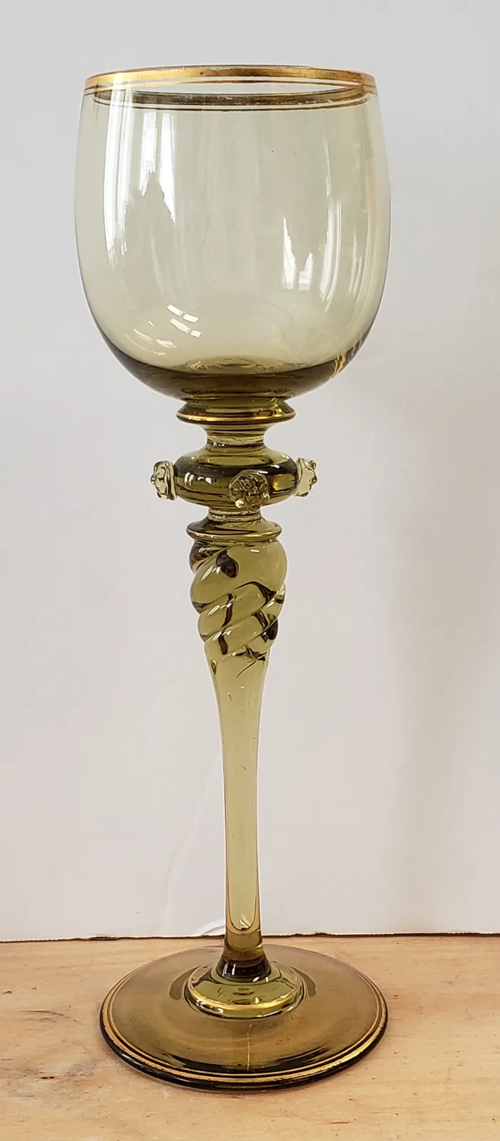 a tall, ornate, amber-colored wine glass with gold trim on the rim and base, a twisted stem with decorative elements, and a…
