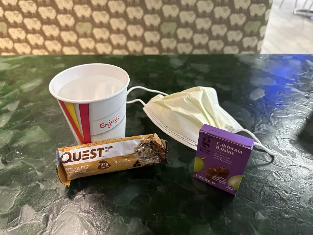 A photo shows a white paper cup with 'Enjoy!' printed on it, a partially eaten Quest chocolate chip cookie dough protein…