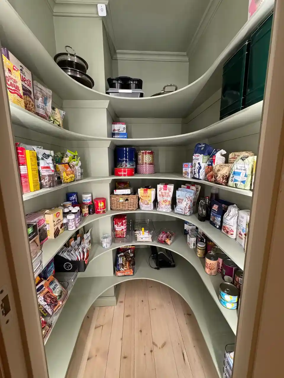 A curved, multi-tiered pantry with light green shelves is filled with neatly organized food items, including canned goods…
