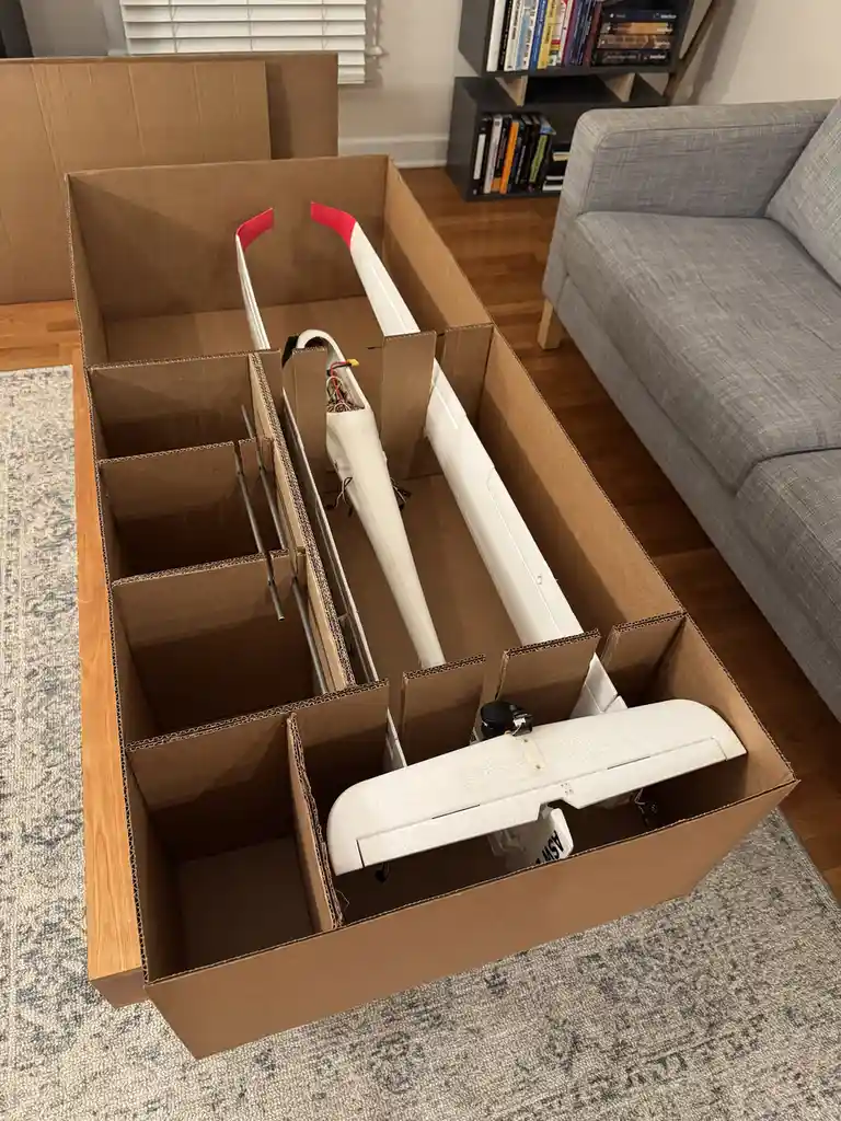 A large cardboard box sits on a rug in a living room, meticulously partitioned with cardboard dividers to securely hold a…