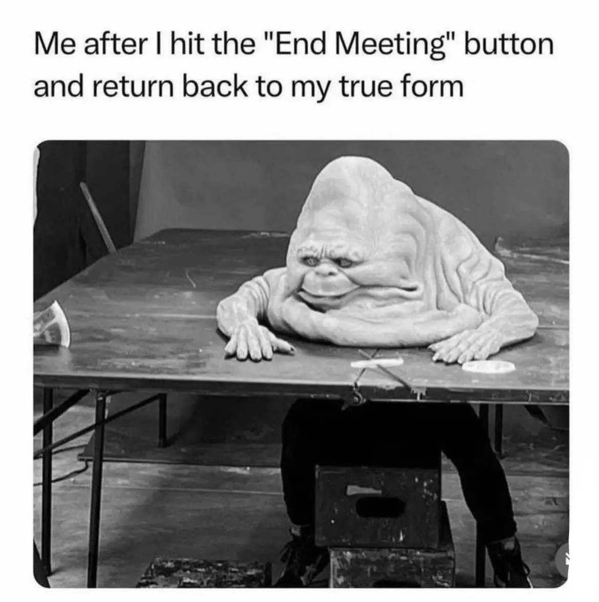 A black-and-white photo shows a person in a Jabba the Hutt costume slumped over a table, with their face pressed against the…