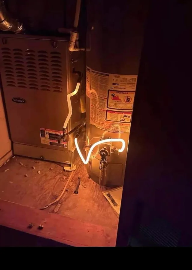 a dimly lit utility room shows a water heater and furnace with a glowing white neon-like line drawn between them, humorously…