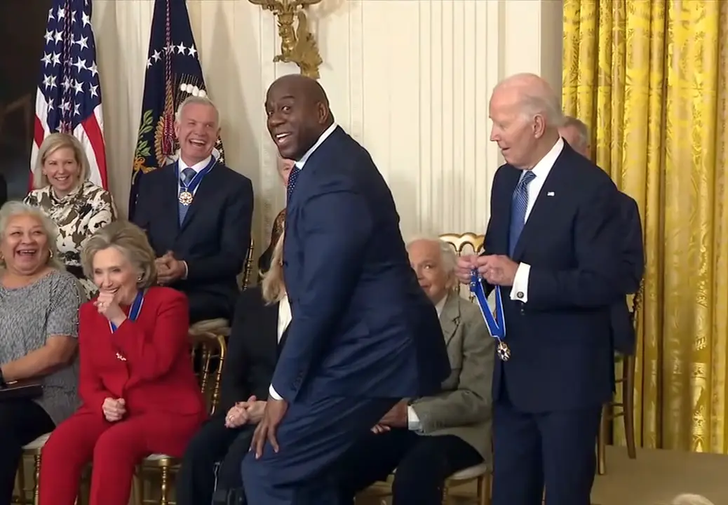 a man in a dark suit is captured mid-squat in a formal room with american flags and golden curtains, while president biden…