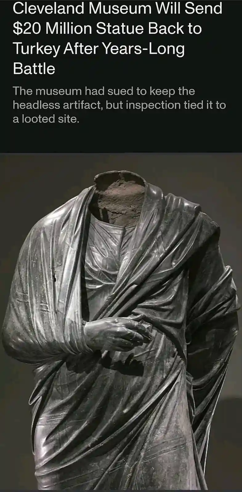 The image shows a headless, ancient-looking statue draped in a toga-like garment, with visible hands clasped in front…