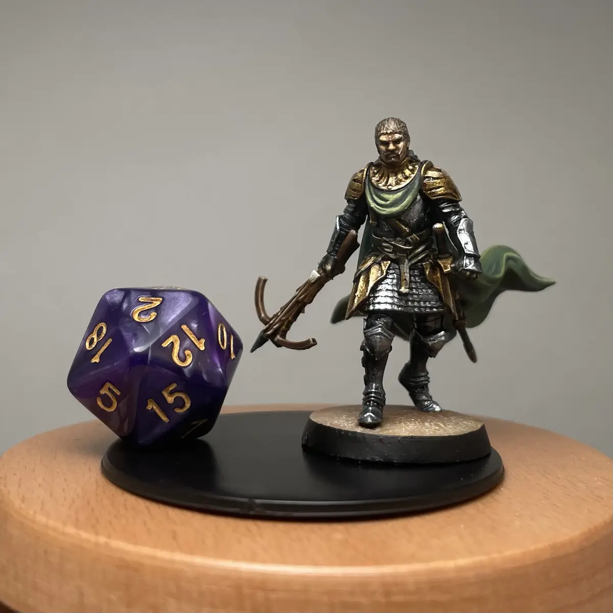 A painted miniature of a fantasy warrior in armor holding a weapon stands next to a large purple 20-sided die showing the…