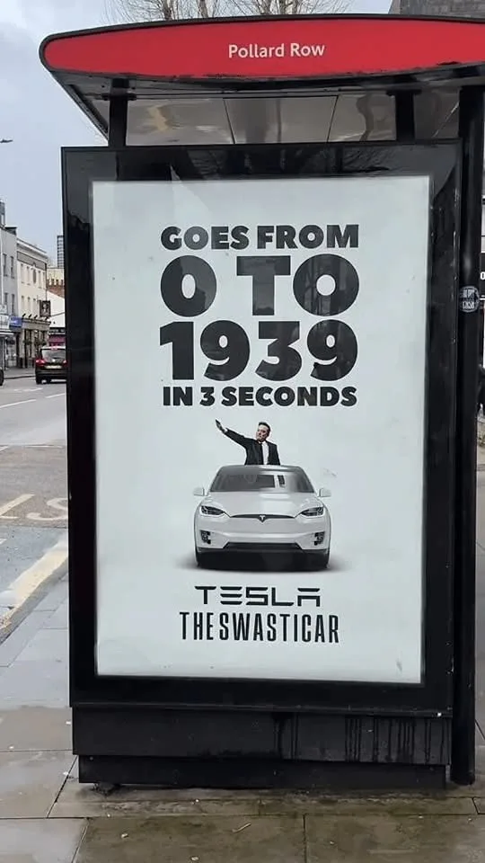 A bus stop advertisement for Tesla features a white car with a man in a suit waving from the roof. The ad claims the car…