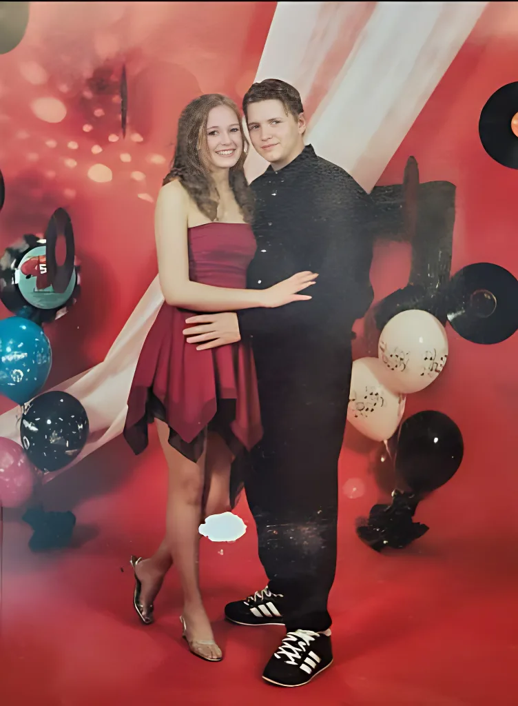 A young couple poses for a formal photo in a red-themed studio with balloons and vinyl records. The woman wears a red dress…