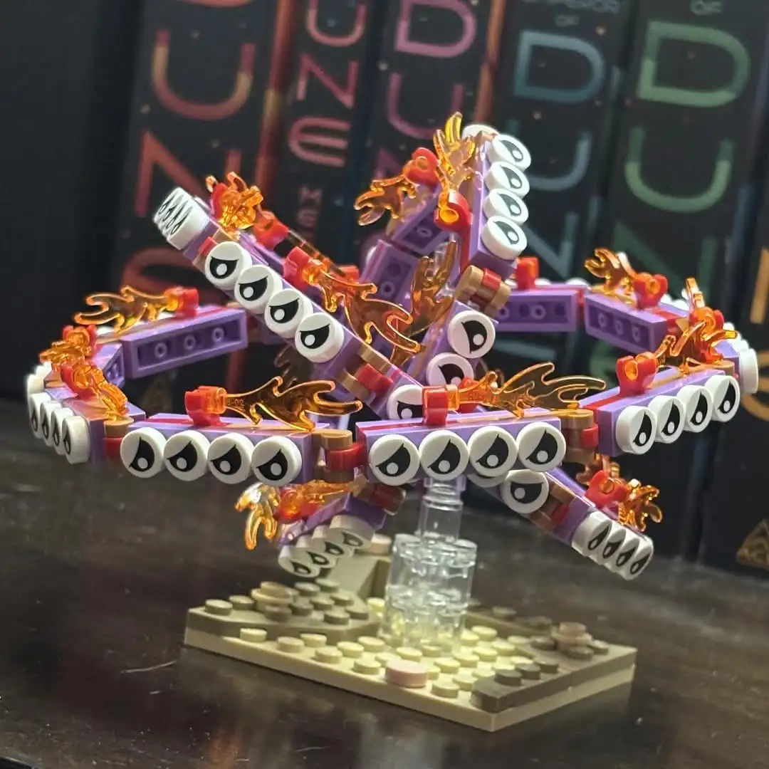 A complex, symmetrical LEGO sculpture resembling a multi-armed, eye-covered creature with orange flame-like pieces, mounted…
