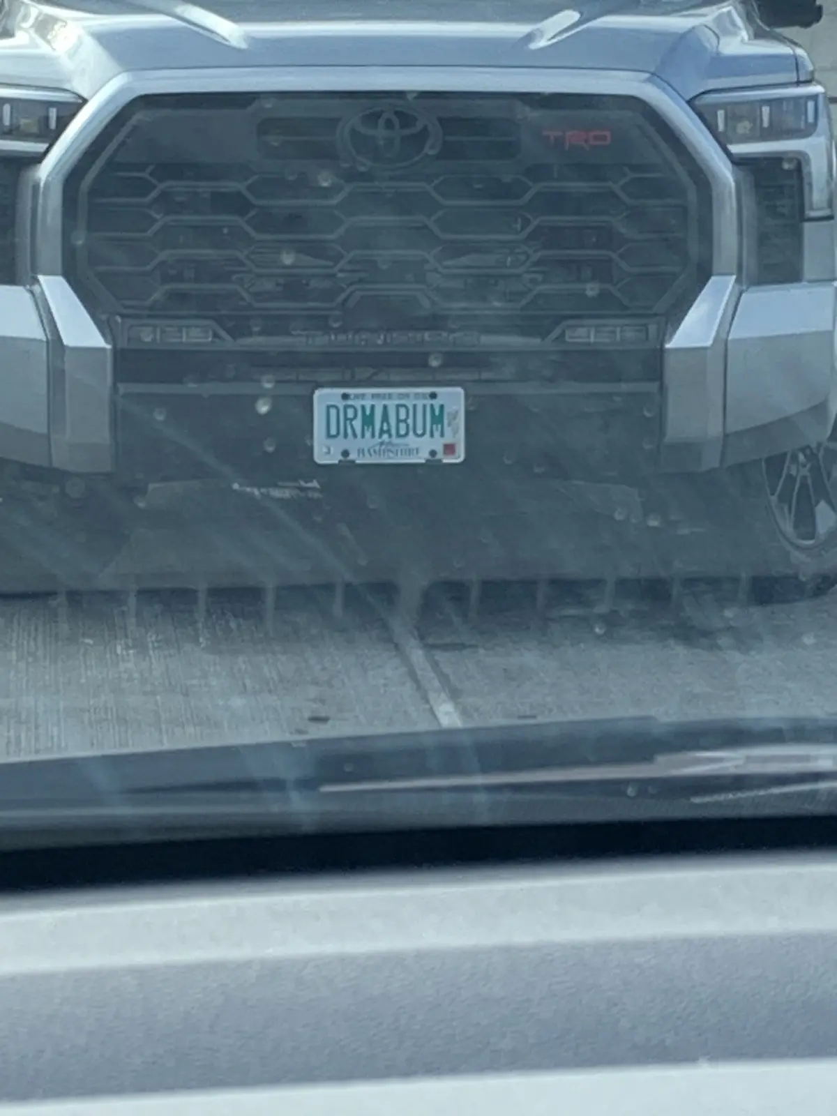 A close-up photo taken from inside a vehicle shows the front of a silver Toyota Tundra TRD pickup truck. The truck's license…