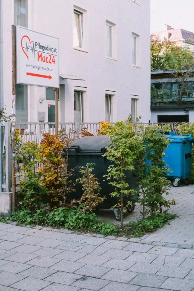 A photo of a white building with a sign reading 'Pflegedienst Muc24' and a website address, with a red arrow pointing right…