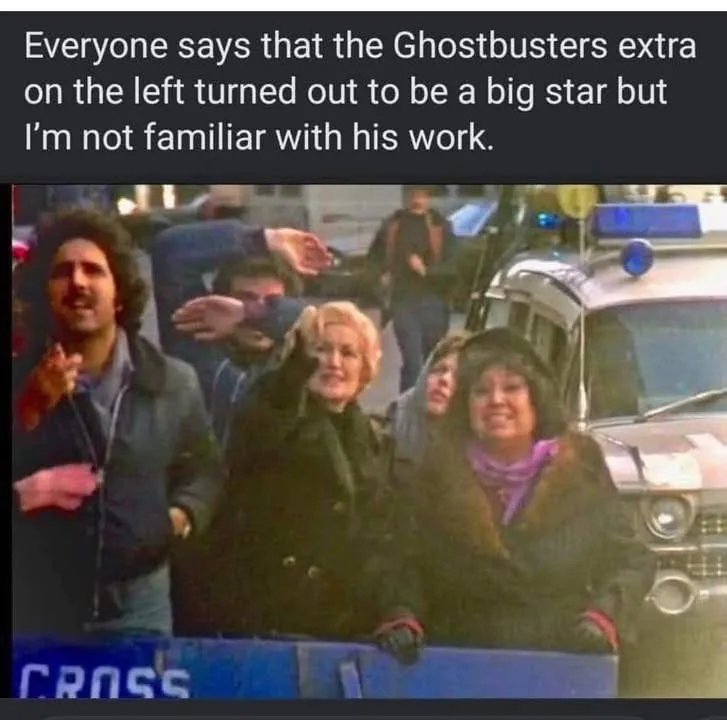 A still from the movie 'Ghostbusters' shows a crowd of extras on a street, with a police car visible on the right. The man…
