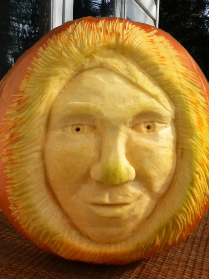 a close-up photo of a pumpkin intricately carved to resemble a man's face with detailed features like eyes, nose, and mouth…