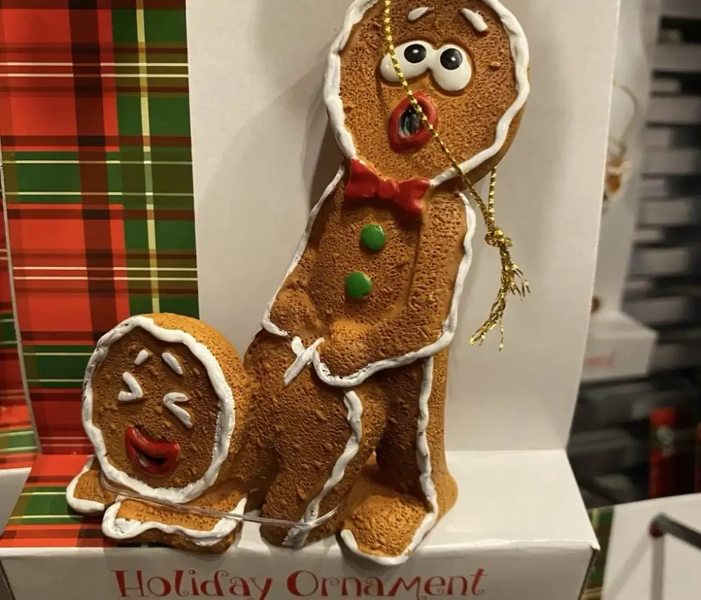 A gingerbread man ornament with a shocked expression sits beside a smaller gingerbread woman ornament with a smug smile…