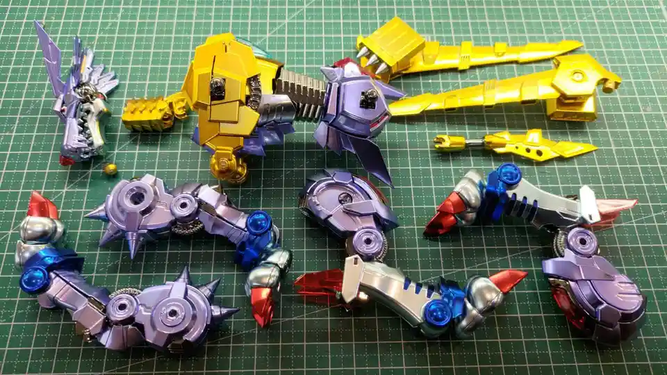 A collection of disassembled, colorful plastic robot toy parts, including limbs and a torso, are scattered on a green grid…