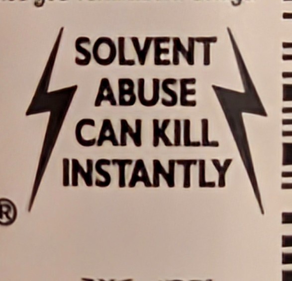 A close-up of a warning label with bold black text stating 'SOLVENT ABUSE CAN KILL INSTANTLY', flanked by two lightning bolt…