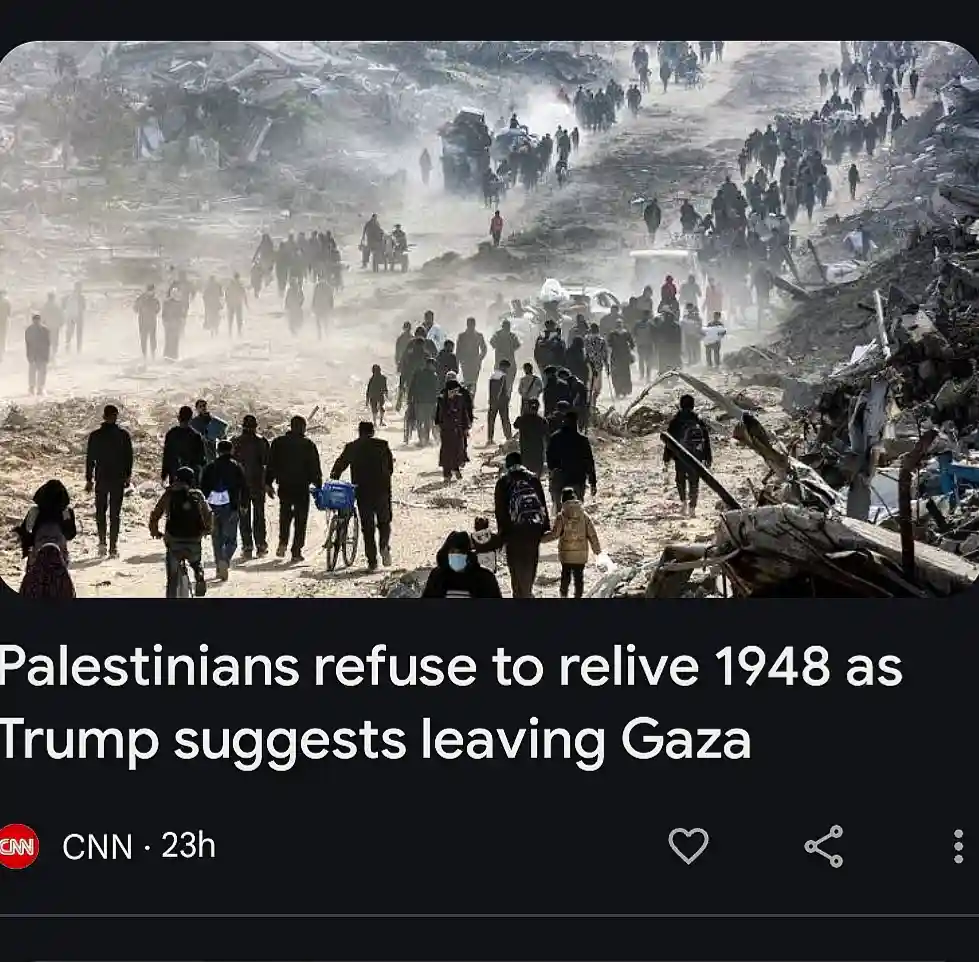 A photo shows a large group of people walking through a devastated, rubble-strewn landscape, carrying belongings and pushing…