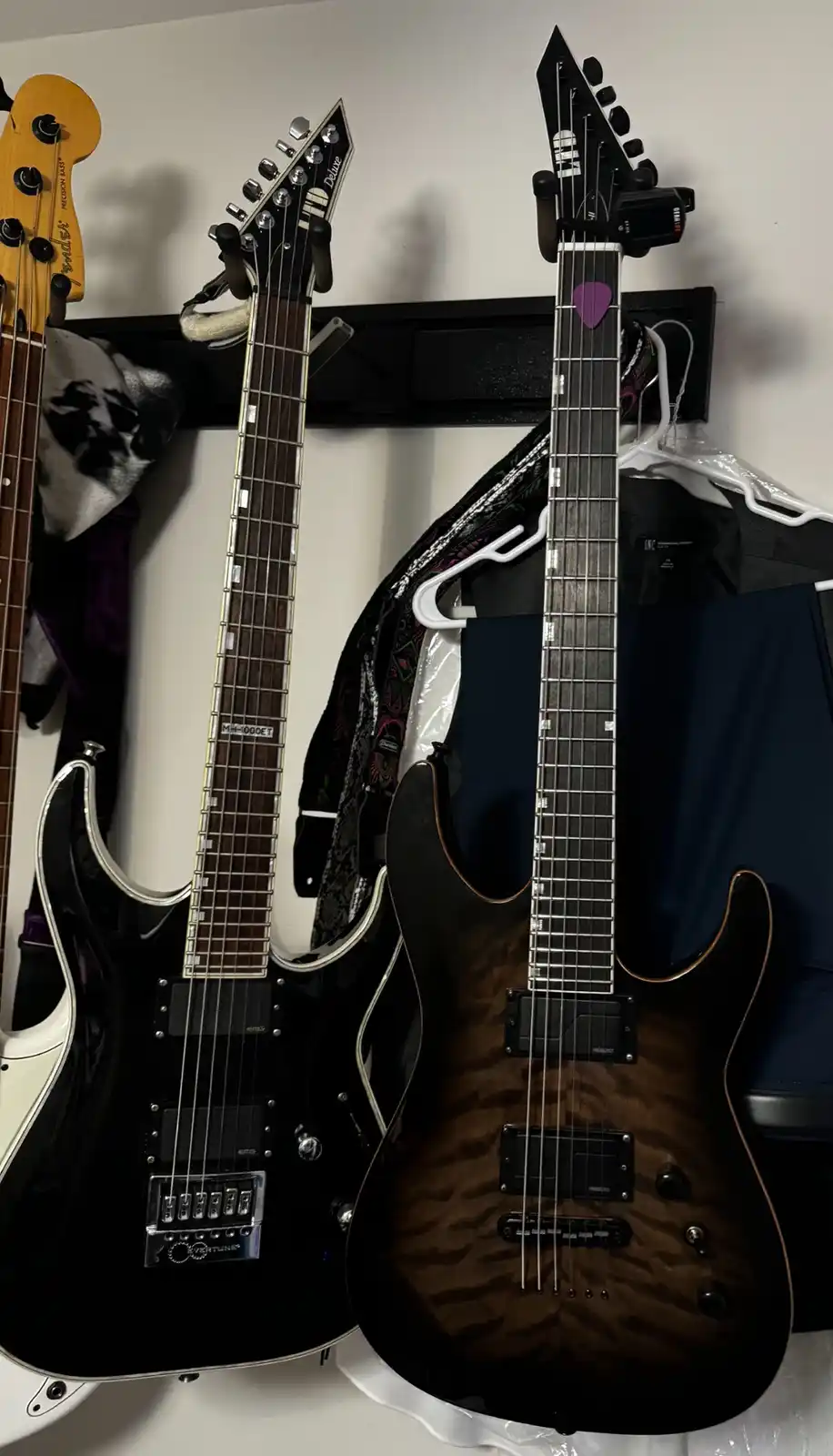 Three electric guitars and a bass are mounted vertically on a wall rack. The leftmost instrument is a Fender Precision Bass…