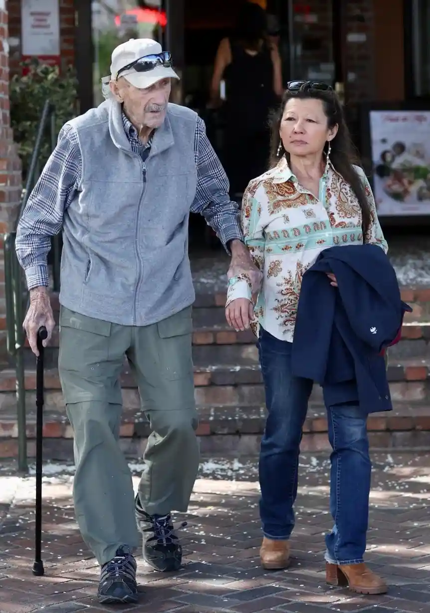 An elderly man with a white cap and sunglasses, holding a cane and walking with a woman, has text overlaid that reads 'i'm…