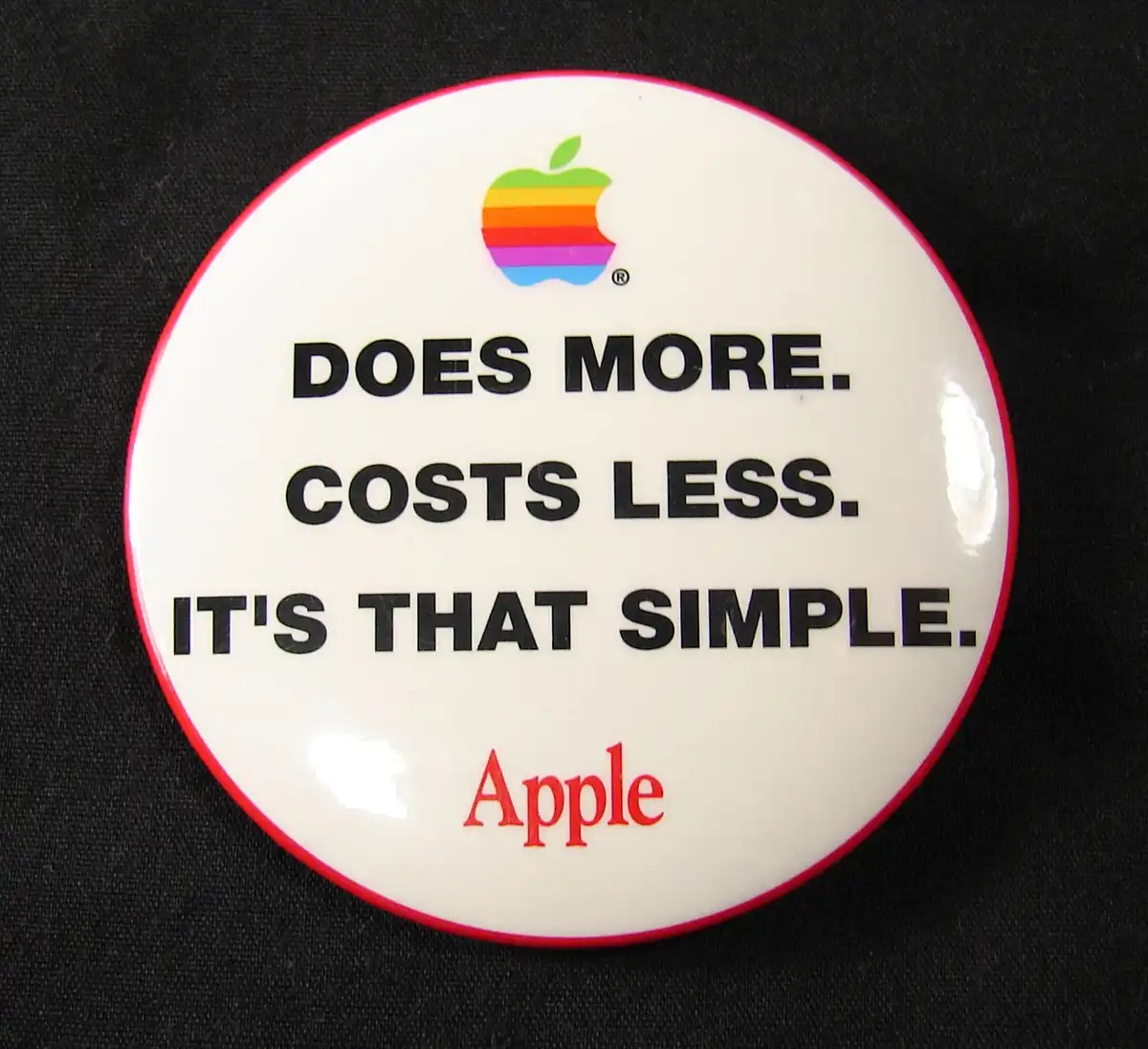 A white circular button with a red border displays the rainbow Apple logo at the top, followed by the text 'DOES MORE. COSTS…