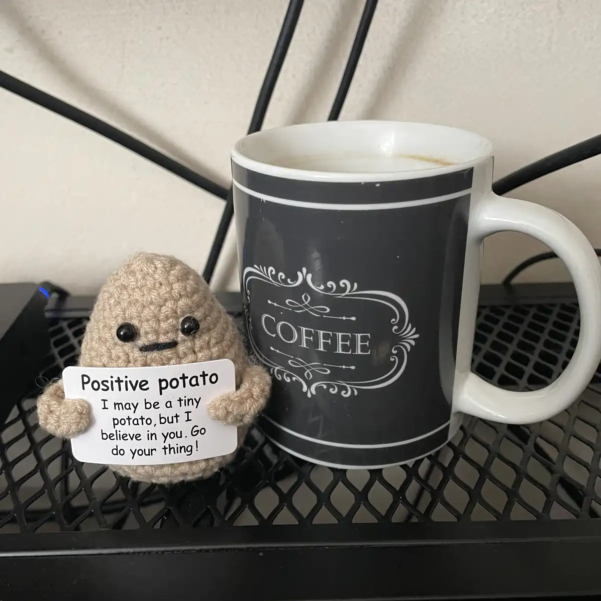 A beige crocheted potato plushie holding a sign that reads 'Positive potato I may be a tiny potato, but I believe in you. Go…