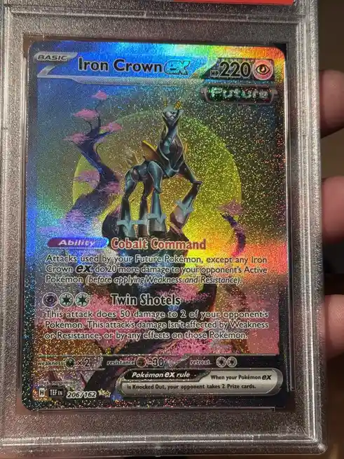 A close-up photo of a Pokémon TCG card for 'Iron Crown EX' with 220 HP, featuring a metallic blue and gold robot-like…