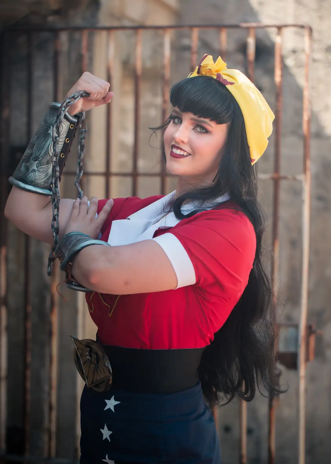A woman in a red, white, and blue costume with a yellow headscarf and star-patterned skirt poses confidently while holding a…