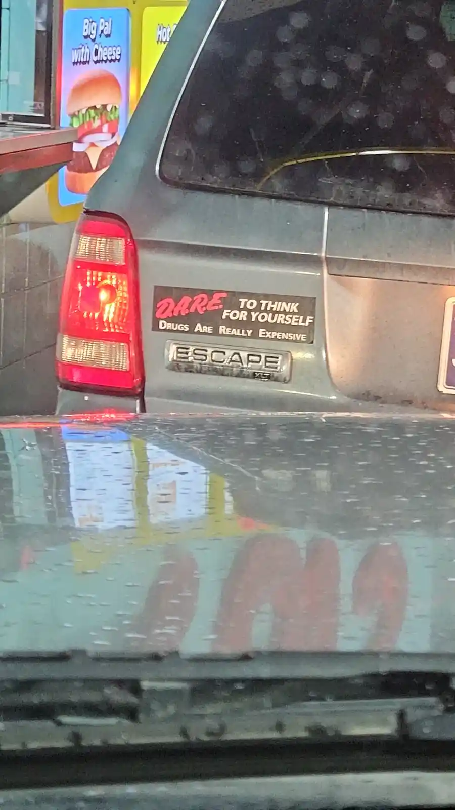 The image shows the rear of a gray Ford Escape SUV with a sticker that reads 'DARE TO THINK FOR YOURSELF DRUGS ARE REALLY…