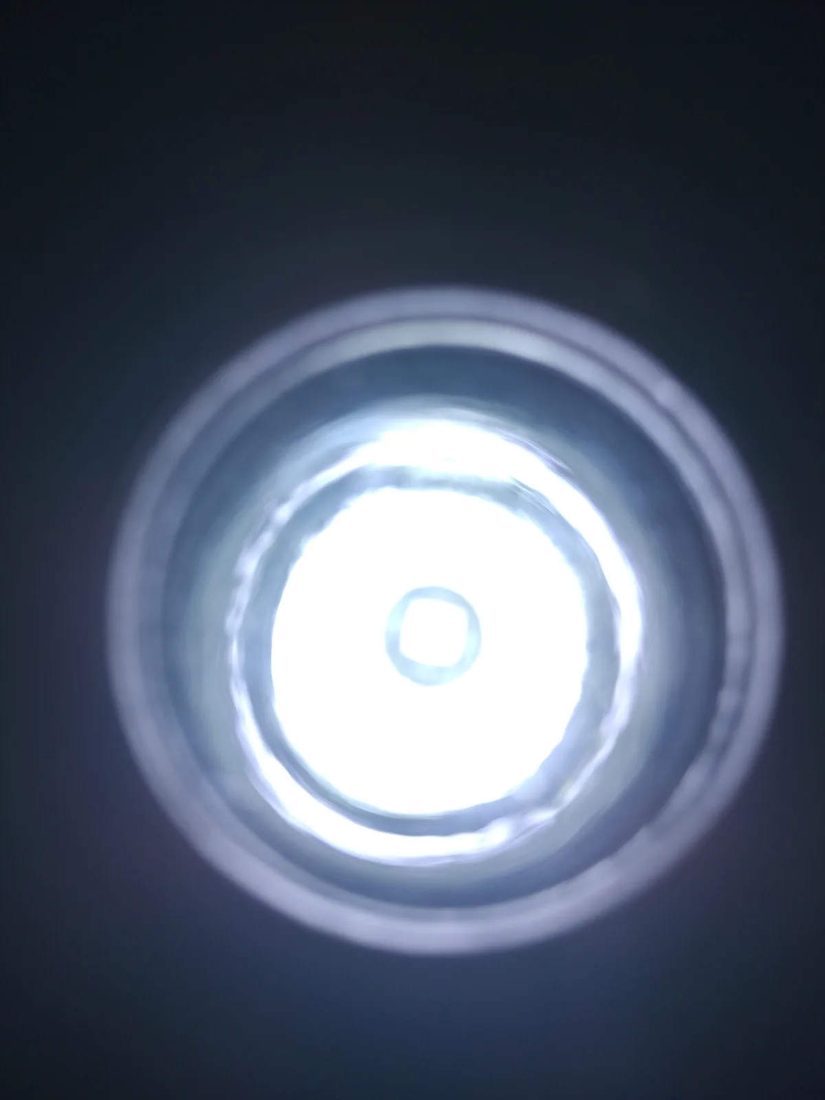A close-up photo shows a bright, circular ceiling light fixture with multiple concentric rings of illumination against a…