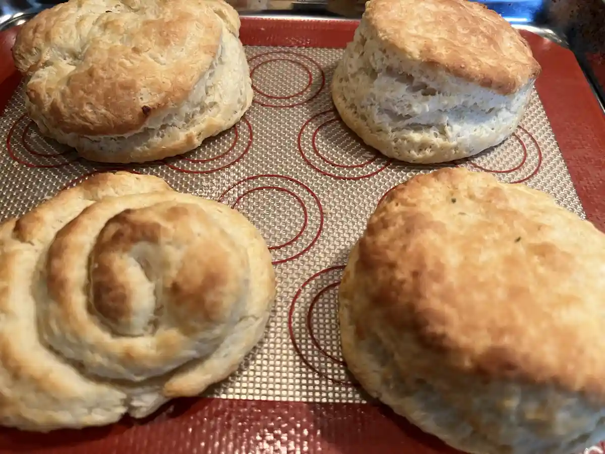 Four golden-brown baked biscuits sit on a red silicone baking mat with circular guides. One biscuit in the bottom left has…