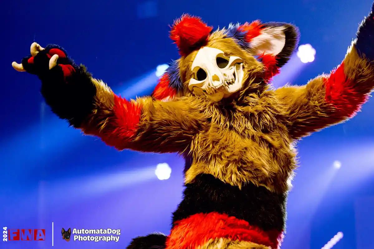 A person in a furry costume with a skull mask and red, black, and tan fur, arms raised in a triumphant pose against a blue…