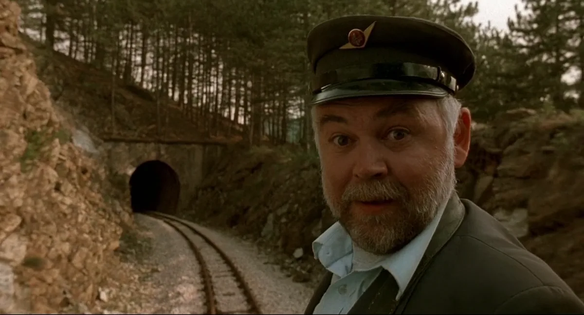 A man in a train conductor's uniform and cap stands beside railway tracks leading into a tunnel, looking directly at the…