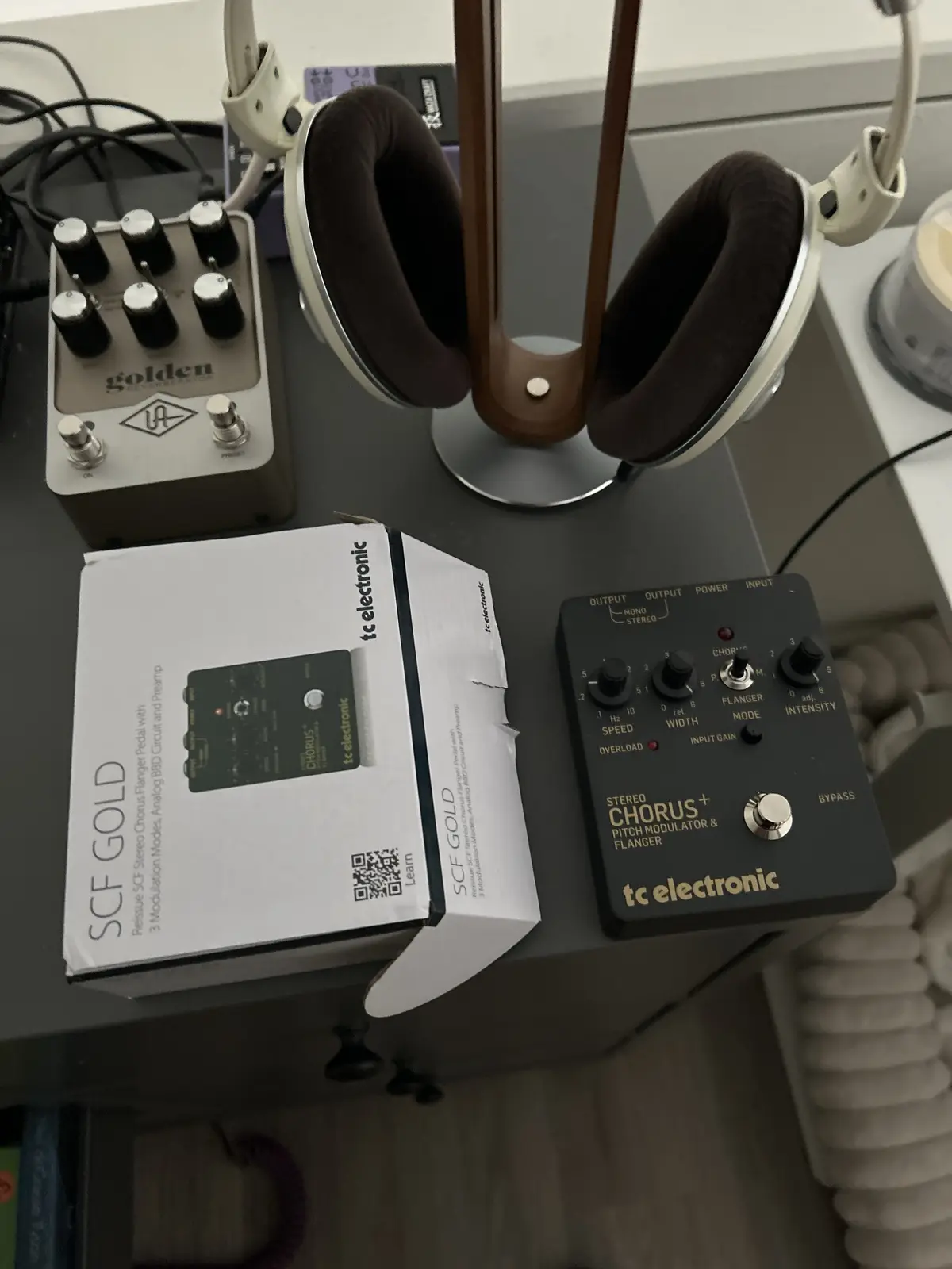 A photo shows a tc electronic SCF Gold guitar pedal box sitting next to the actual pedal on a desk, with a pair of…