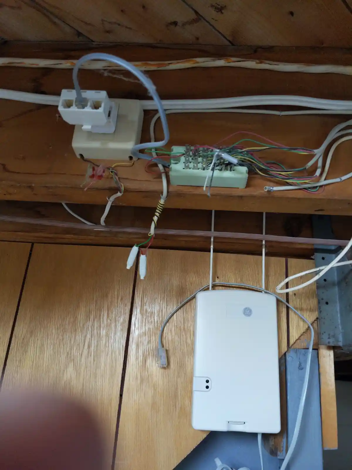 A messy, tangled mess of wires and connectors is visible on a wooden surface, with a white GE-branded device hanging below…