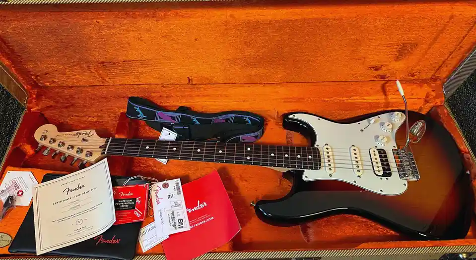A Fender Stratocaster electric guitar rests in its open, orange-lined case, surrounded by official Fender paperwork…