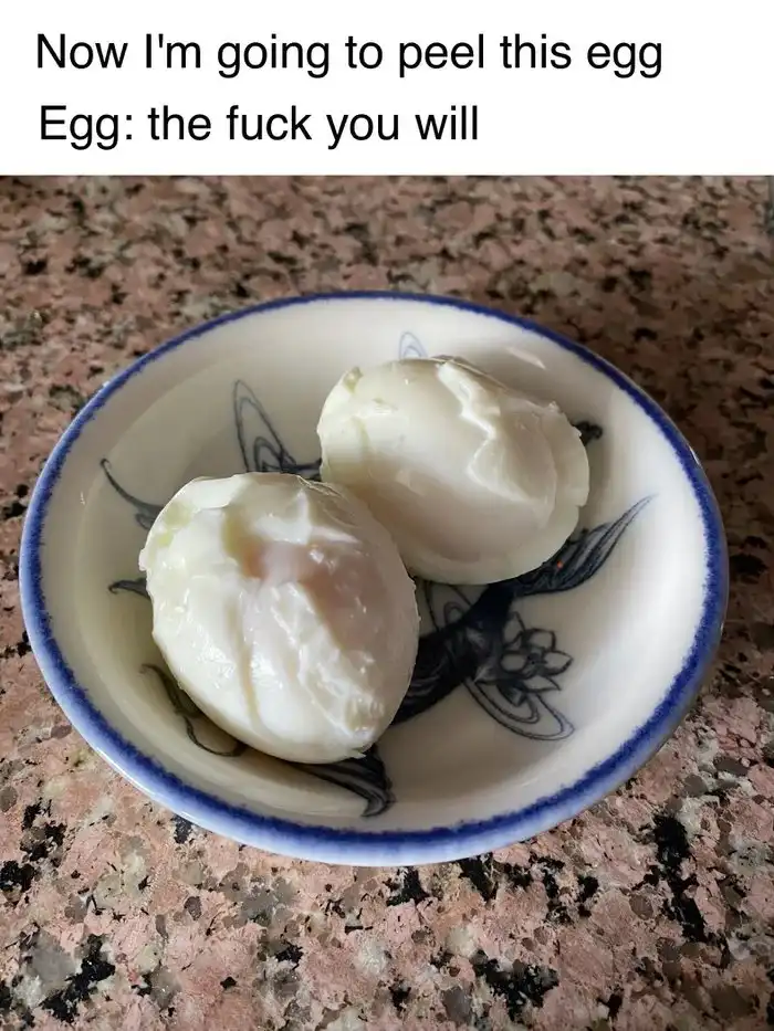 Two peeled hard-boiled eggs sit in a small white ceramic bowl with blue floral patterns, resting on a speckled pink and…