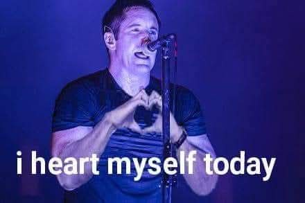 A man, likely a singer, is shown on stage under blue lighting, making a heart shape with his hands around a microphone. The…