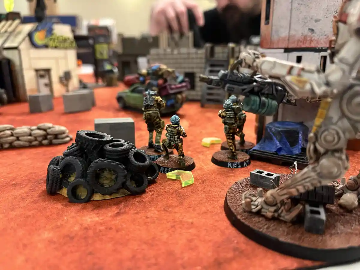 A close-up photo of a tabletop wargaming setup with miniature figures, including a large robot and several soldiers…