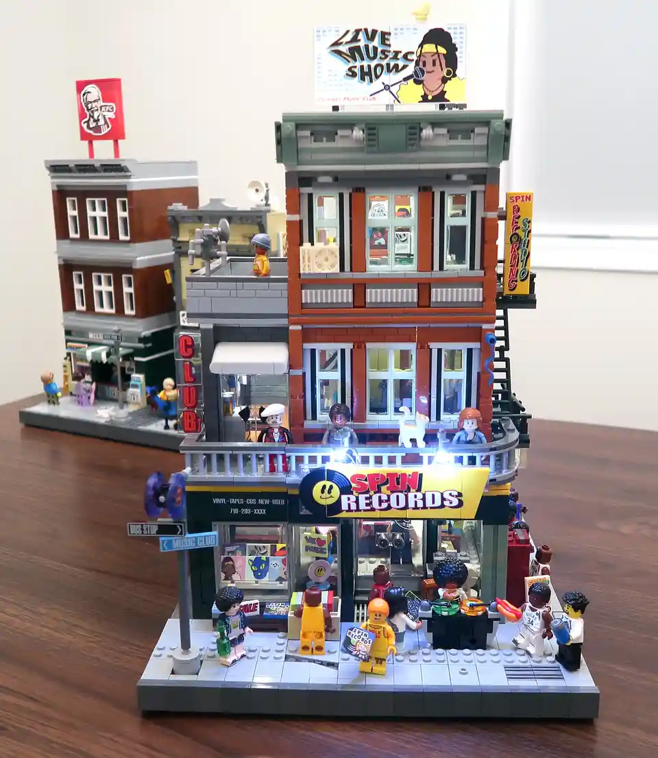 A detailed LEGO diorama of a street corner featuring a 'Spin Records' music store with a 'Live Music Show' sign above and a…
