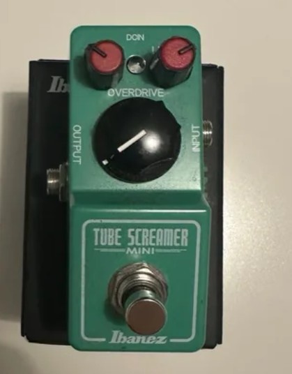 A green Ibanez Tube Screamer Mini guitar effects pedal with red knobs, a black control knob, and a footswitch, with the text…
