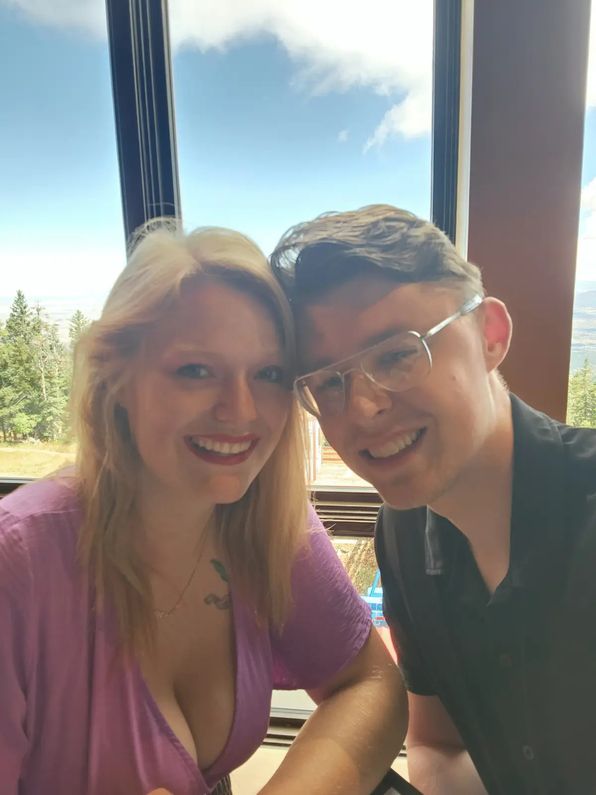 A selfie of a smiling blonde woman in a purple top and a smiling man with glasses, both looking at the camera with their…