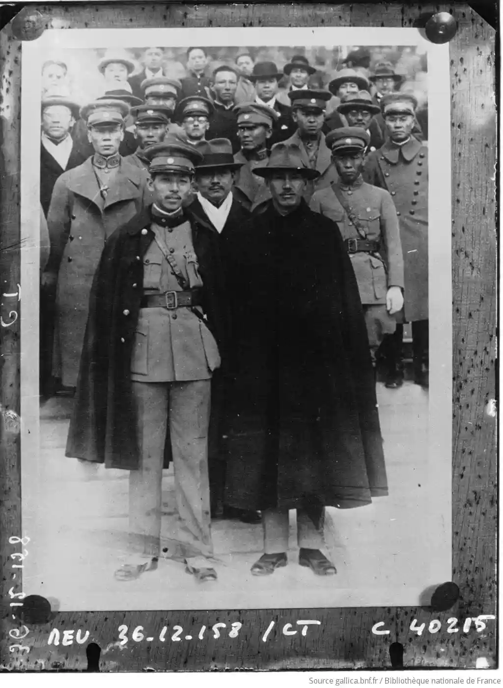 a vintage black-and-white group photograph of men in early 20th-century military and civilian attire, with one man in the…