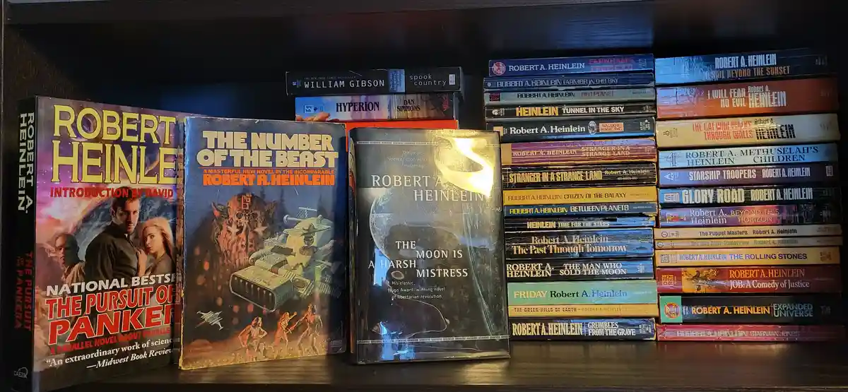 A bookshelf displays numerous science fiction novels, mostly by Robert A. Heinlein, with 'The Moon Is a Harsh Mistress'…