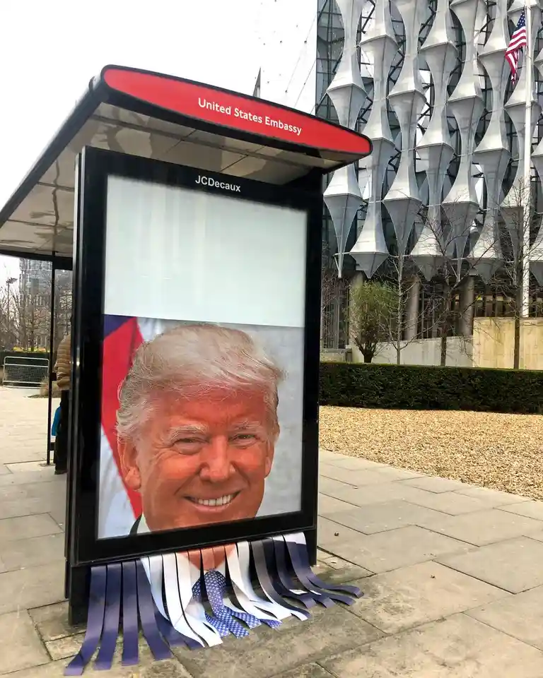A photo shows a bus shelter with a JCDecaux advertisement displaying a smiling portrait of Donald Trump, with his tie and…