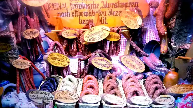 A vibrant display of German sausages at a market stall, with numerous types of sausages hanging and arranged in baskets…