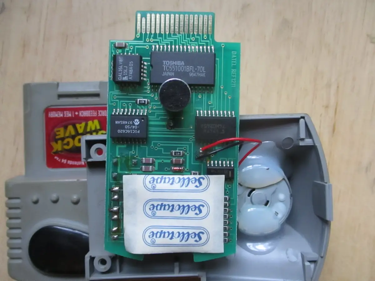 A disassembled Nintendo 64 game cartridge with its internal green circuit board exposed, showing various chips and…