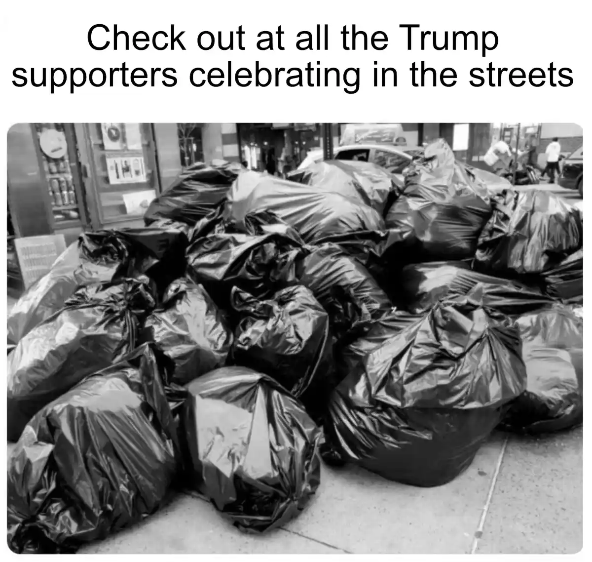 A black-and-white photo shows a large pile of black trash bags on a sidewalk, with a vending machine and street scene in the…